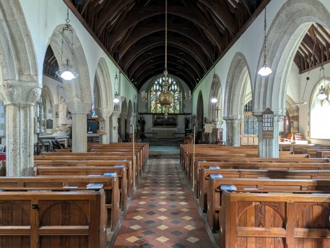 Interior view of a church showcasing wooden pews, stone arches, and a high ceiling with exposed beams, leading towards an altar at the front.