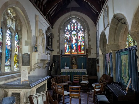 Interior view of a church featuring stained glass windows, wooden chairs, and an altar.